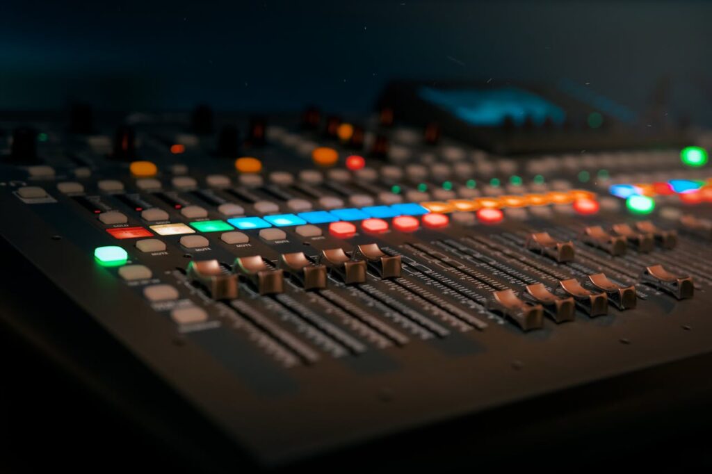 pexels-photo-3784566 Close-up of a professional sound mixer with colorful glowing controls in a dimly lit studio.